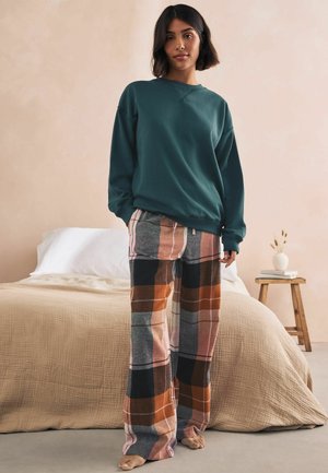 Türkis sweatshirt, millel ümar kaelus, mis on kombineeritud ruuduliste, laia säärega pükstega, millel on oranžid, hallid ja roosad toonid. Pehmed tekstuurid on nähtavad.