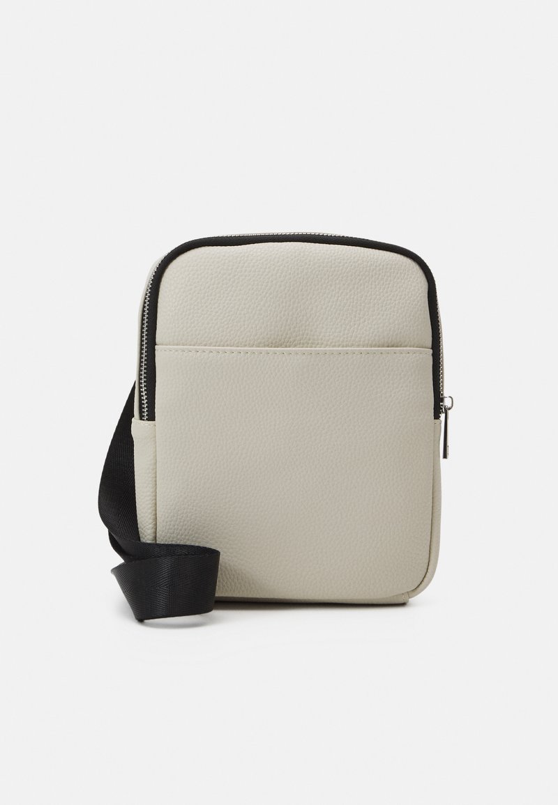 Cream-colored crossbody bag with textured surface, zipper closure, and black strap. Features a front pocket for extra storage.