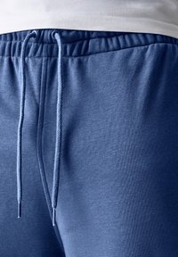 Pantalons de jogging athlétiques bleus en tissu doux, dotés d'une taille élastique avec cordon de serrage, d'une texture lisse et de coutures minimales.