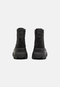 Sneakers alte nere con una parte superiore in tessuto texturizzato, suola di gomma spessa, linguetta posteriore e marchio in rilievo sul tallone.
