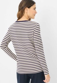 Lange mouwen T-shirt in crème met donkerblauwe horizontale strepen. Zachte stof, ronde halslijn en getailleerde pasvorm. Effen achterkant zonder extra details.