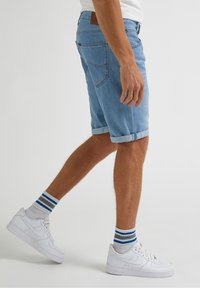 Ljusblå denimshorts med uppvikt nederkant, i kombination med vita sneakers och randiga strumpor. Den övergripande stilen är avslappnad och ledig.