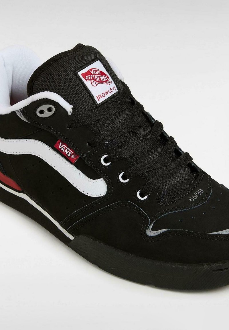 Zwarte suède skate schoenen met witte accenten, voorzien van een gevoerd kraagje, zwarte veters, perforaties aan de zijkanten en een rode label op de hak.