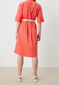 Abito camicia corallo con cintura a motivo floreale, maniche corte e taglio a lunghezza ginocchio. Tessuto di cotone morbido con una vestibilità rilassata.