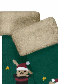 Grüne Socken mit einem plüschigen, beigen Bündchen, das ein gestricktes Muster eines Hasen mit einer Weihnachtsmütze und Sternen zeigt. Weicher Stoff überall.