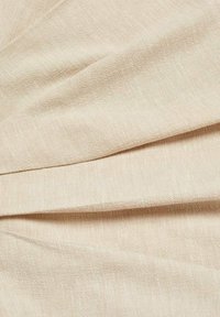 Vaaleanbeige kangas, jossa on sileä pinta ja hillitty kiilto, sisältää vinon laskoskuvioinnin lisäulottuvuuden ja visuaalisen kiinnostavuuden luomiseksi.