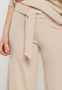 Beige Strickhose mit weitem Bein, ausgestattet mit einem selbstgebundenen Gürtel in der Taille und einem weichen, strukturierten Stoff.