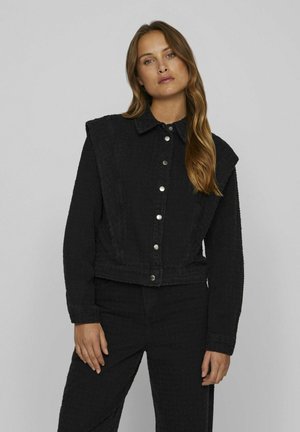 Veste noire courte en tissu texturé, avec un col pointu, une fermeture à bouton et un design d'épaule prononcé.