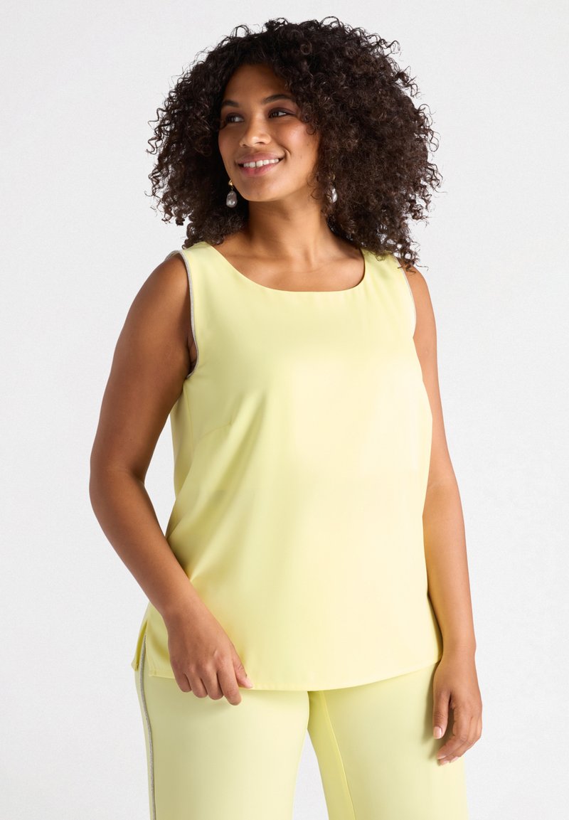 Top giallo senza maniche con scollatura rotonda, texture liscia e spacchi laterali, abbinato a pantaloni gialli coordinati.