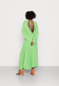 Abito verde a maniche lunghe e schiena scoperta realizzato in tessuto leggero, con gonna fluida e sandali con tacco blocco arancioni.