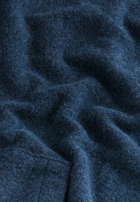 Donkerblauwe wollen stof met een zachte, pluizige textuur en zichtbare plooien en stiksels aan de linkerbenedenrand.