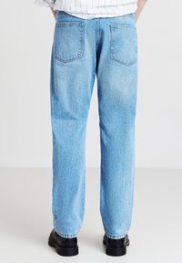 Jeans in denim azzurro chiaro con una vestibilità rilassata, dotati di tasche posteriori e un design a gamba dritta. Dettagli di cucitura visibili lungo le cuciture.