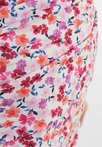 Tela floral con pequeñas flores rosas, rojas y moradas sobre un fondo blanco, con una textura suave y un ligero detalle fruncido.