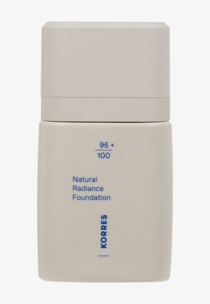 Korres Luonnollinen Hehkua Antava Meikkivoide, jossa on matta beige pullo pyöreällä kannella. Pullo sisältää sinistä tekstiä tuotedetailsiin ja logoa varten.