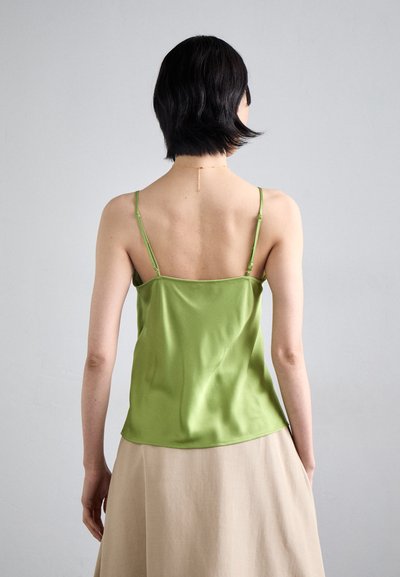 Green satin camisole with thin straps, smooth texture, and a relaxed fit, paired with a light beige skirt. Gold chain necklace visible.
