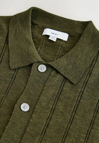Polo en maille vert olive avec col, deux boutons blancs, rayures verticales en maille ajourée et étiquette "NEXT" taille moyenne.