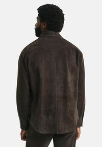 Bruine suède shirt met een ontspannen pasvorm, voorzien van een achterpand detail, lange mouwen en een rond afgewerkte zoom. De textuur is zacht en licht geborsteld.