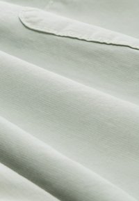 Jasnozielony materiał o drobnym wzorze teksturowym, z gładkimi fałdami i lekko błyszczącym wykończeniem. Materiał wydaje się miękki i lekki.