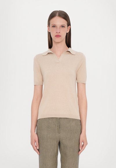 Camisa polo de manga corta beige con escote en V y diseño con cuello, hecha de un material suave, combinada con pantalones de cuadros verdes y negros.