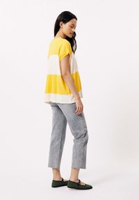 Geel en wit gestreepte, losse top gecombineerd met lichtgrijze jeans met rafelige zomen, en groene flats met een zwarte rand.