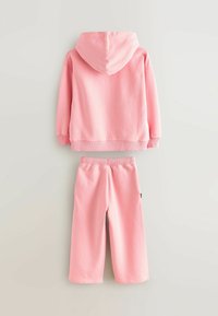 Ensemble de deux pièces rose avec un haut à manches longues à capuche et un pantalon ample, présenté à plat sur un fond neutre.