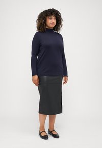 Navyblaues Langarm-Turtleneck-Oberteil, kombiniert mit einem schwarzen, gefälschten Leder-Bleistiftrock mit seitlichem Schlitz, abgerundet mit schwarzen Mary Jane Schuhen.