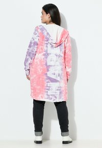 Sudadera larga de tie-dye en tonos rosa y morado, con una gran impresión blanca de "HAPPY" en la parte posterior. Fabricada en tela suave, con un bolsillo tipo canguro y capucha.
