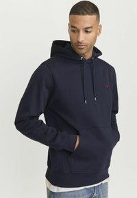 Haut à capuche bleu marine en tissu doux, avec une poche avant, un capuchon à cordon réglable et un petit logo rouge sur la poitrine.