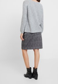 Maglione grigio a maglia con maniche lunghe, abbinato a una gonna a quadri bianco e nero. Stivaletti neri completano il look.