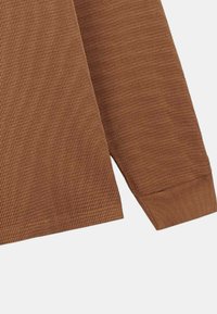 Chemise à manches longues texturée marron avec un motif en grille ; dotée d'un poignet et d'un ourlet côtelés, affichant une apparence structurée et confortable.