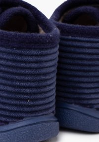 Pantofole blu navy con upper a costo rib nelle trama e suola in gomma solida, caratterizzate da punte arrotondate e un interno morbido e peloso.