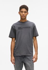Szara bawełniana koszulka z krótkim rękawem, z logo "KARL LAGERFELD JEANS" w czerni na piersi. Prosta, ściągająca u dołu i okrągły dekolt.