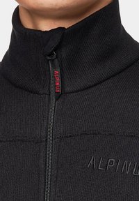 Czarna polarowa kurtka z zamkiem błyskawicznym i wysokim kołnierzem, wykonana z teksturowanej tkaniny, z logo "ALPINUS" w kolorze czerwonym na uchwycie zamka oraz z misternymi detalami przeszycia.