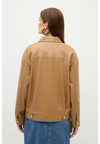 Brun kunstlæderjakke med spidse krave, dekorative øjer og trykknapmanchetter. Designet har rene linjer og en afslappet silhuet.