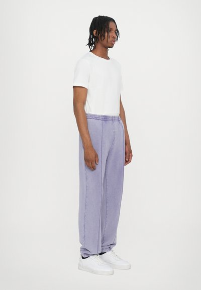 Lightweight, purple sweatpants with an elastic waistband and cuffed ankles, paired with a fitted white t-shirt and white sneakers.
