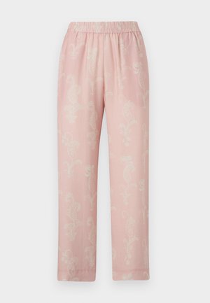 Naine, kes kannab lahtist kahvaturoosat pluusi ja sobivaid laiu lilli mustriga pükse, millele on lisatud mustad madalad kingad.