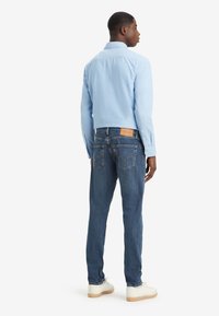 Cămașă bleu deschis, din bumbac, asociată cu blugi negri din denim, cu buzunare pe spate și accente din piele bej. Tenisi completează ținuta.