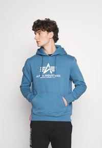 Felpa con cappuccio blu in cotone, dotata di tasca a marsupio frontale, stampa del logo bianca e polsini a coste. Pantaloni neri con logo bianco.