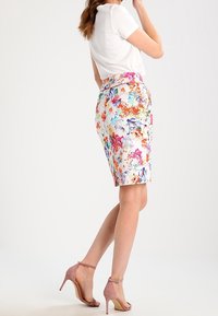 Květinová tužková sukně z lehkého materiálu s velmi barevnými vzory, spárovaná s bílým topem s krátkým rukávem a růžovými sandály na kotníkovém pásku.