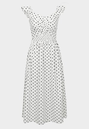 Fehér ruha fekete pöttyökkel, smocked mellrésszel, fodros vállpántokkal és laza szoknyával, amely megkönnyíti a mozgást.