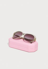 Ochelari de soare cu un cadru gri translucid, lentile gradient de culoare purpurie și accente aurii, așezați pe un toc rectangular roz cu o suprafață texturată.