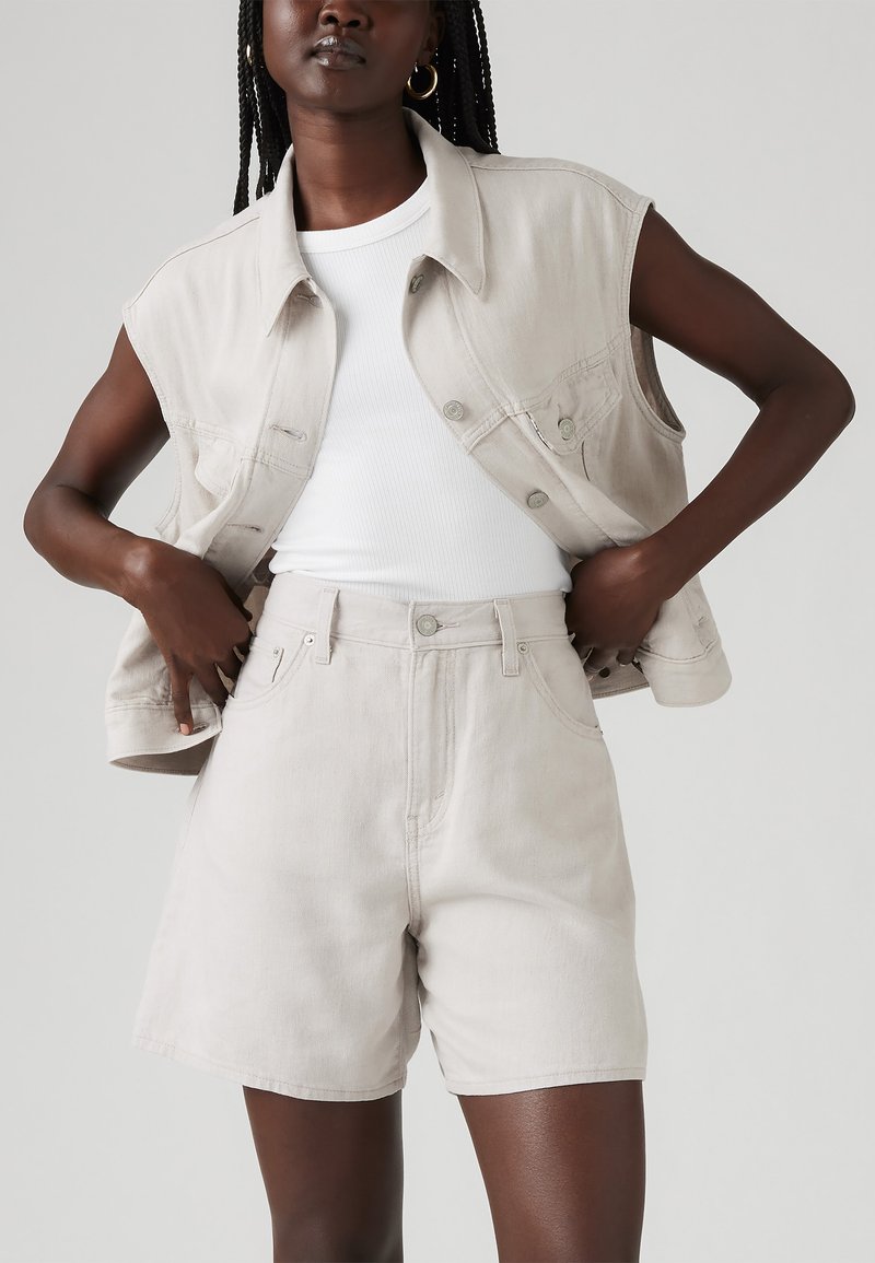 Helles beiges Jeansweste mit ärmellosem Design und Knöpfen auf der Vorderseite, kombiniert mit hochgeschnittenen, hellbeigen Shorts. Glatte Textur, lässiger Schnitt.