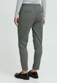 Kalhoty s houndstooth vzorem v černobílé kombinaci, elastickým pasem a bočními kapsami. Nosené s černými plochými botami.