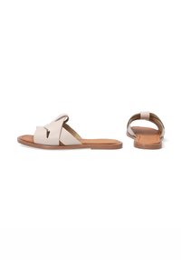 Beige leren slide sandalen met kruiselings gespen, platte tan kleurige zool, open achterkant ontwerp, gladde textuur, met minimalistische hardware.