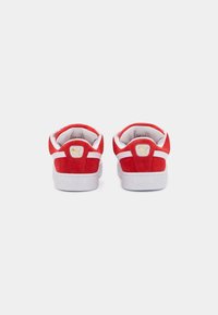 Red suede sneakers with white accents, featuring a white rubber sole and a gold logo on the heel. Rounded toe and padded collar.
