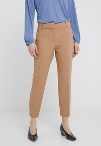Pantalons beige ajustés avec une coupe slim, dotés d'une taille mi-haute et de poches avant cousues. Associés à un haut à manches longues bleu clair et des escarpins noirs.