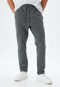 Pantaloni jogger grigi realizzati in tessuto morbido, con vita con coulisse, design a gamba affusolata e polsini elasticizzati, abbinati a sneakers bianche.