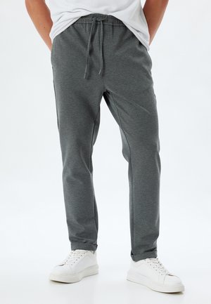 Grå joggebukser lavet af blødt stof med snor i taljen, tætsiddende bendesign og elastiske manchetter, parret med hvide sneakers.