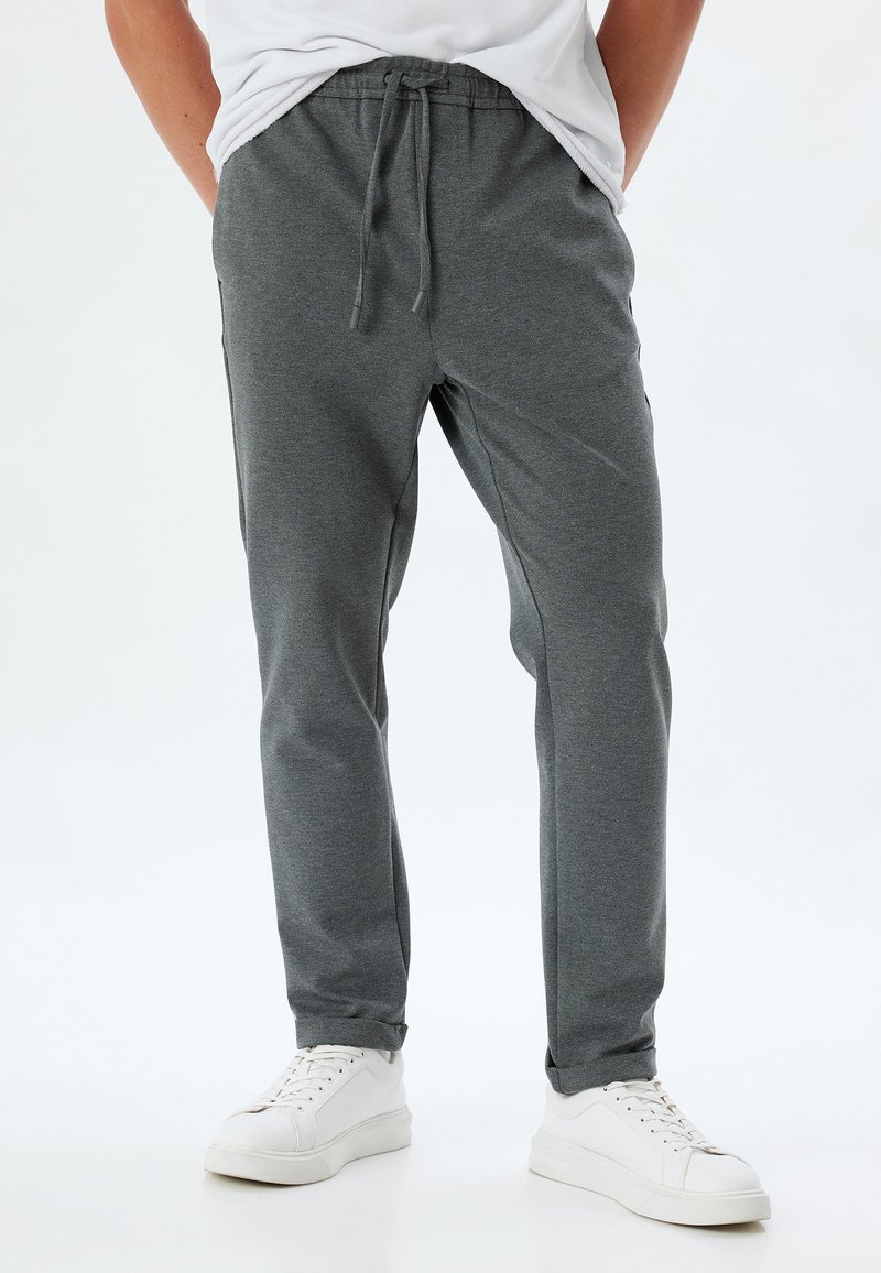Pantaloni jogger grigi realizzati in tessuto morbido, con vita con coulisse, design a gamba affusolata e polsini elasticizzati, abbinati a sneakers bianche.