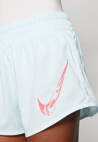 Šviesiai mėlynos sportinės šortai su elastinga juosta ir rožiniu Nike logotipu kairėje pusėje, pagaminti iš lygaus, lengvo audinio.